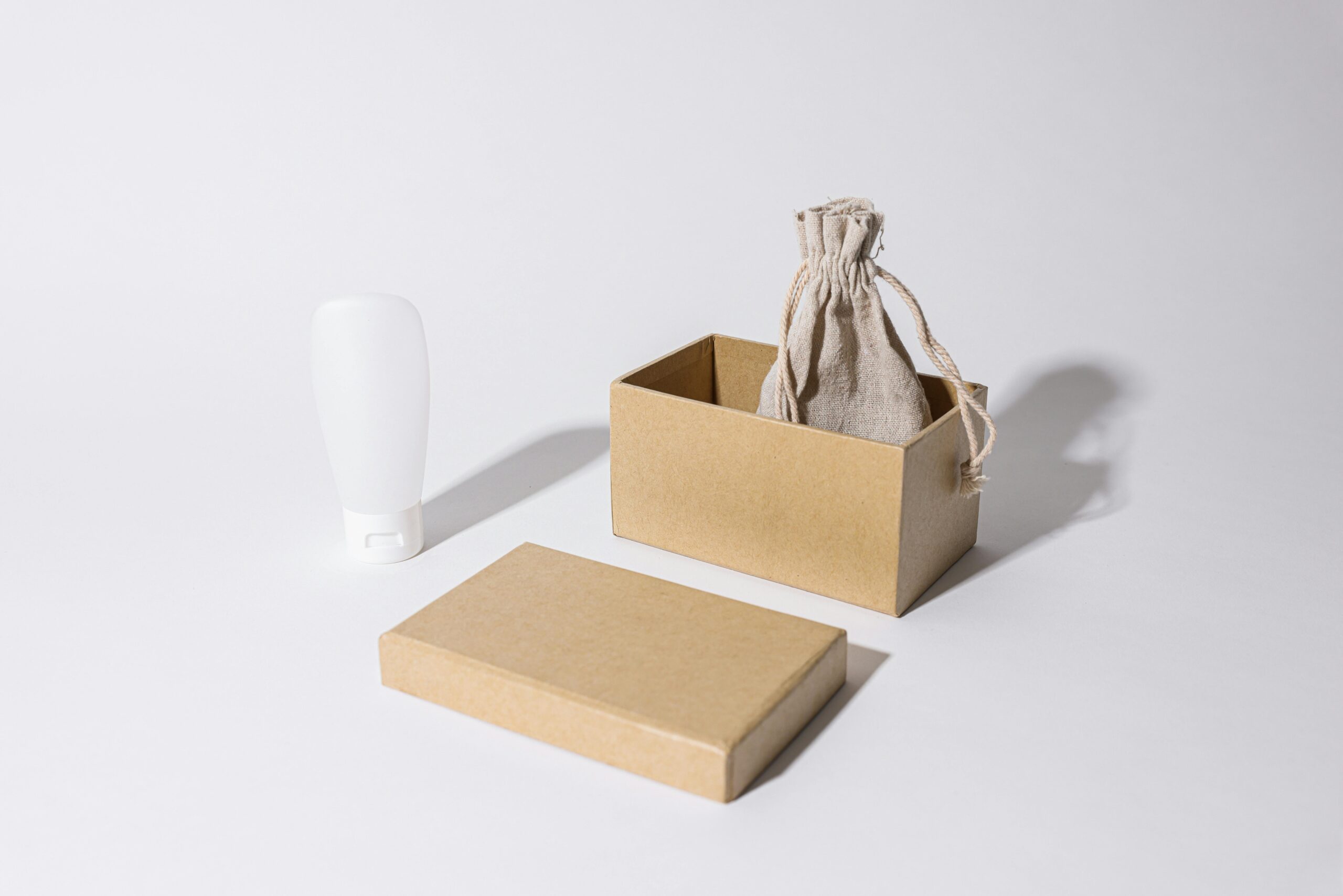 Home Stylish minimalist mockup featuring a cardboard box, linen pouch, and cream tube on a white background.
